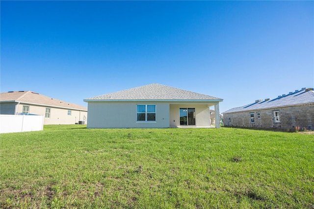 rear view of house featuring a yard, fence, and stucco siding