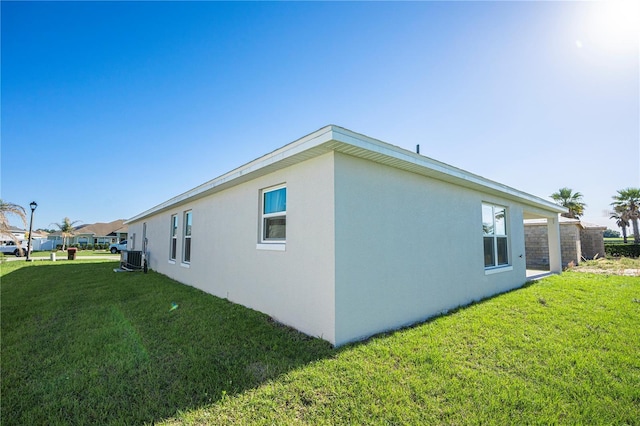 view of side of home with central air condition unit, a yard, and stucco siding