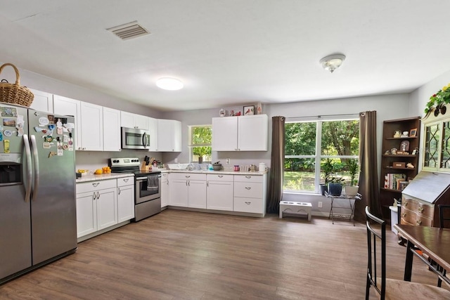 kitchen with appliances with stainless steel finishes, hardwood / wood-style flooring, and white cabinets