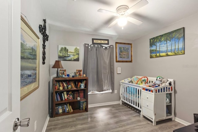 bedroom with ceiling fan, a nursery area, and wood-type flooring