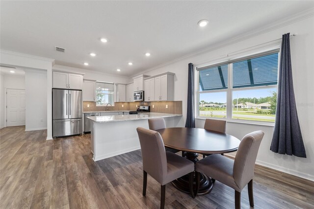 dining room featuring ornamental molding, sink, a healthy amount of sunlight, and dark hardwood / wood-style flooring