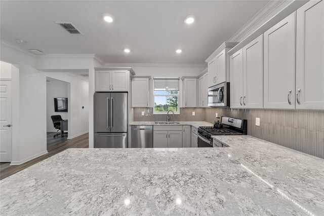 kitchen with sink, appliances with stainless steel finishes, light stone countertops, crown molding, and dark hardwood / wood-style flooring