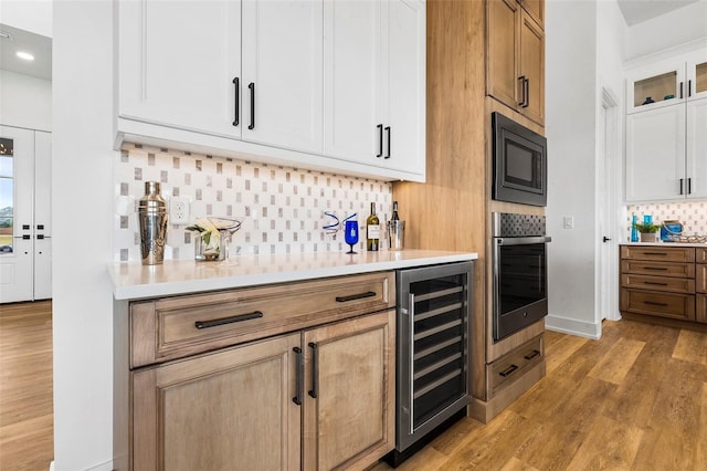 bar with tasteful backsplash, stainless steel oven, white cabinetry, light wood-type flooring, and beverage cooler