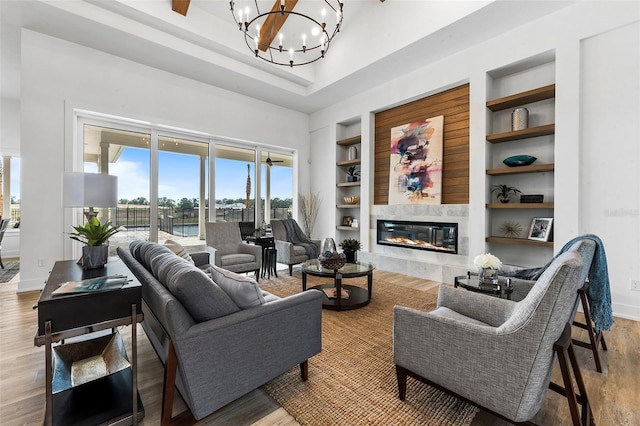 living room with wood-type flooring, an inviting chandelier, built in shelves, a tray ceiling, and a high end fireplace