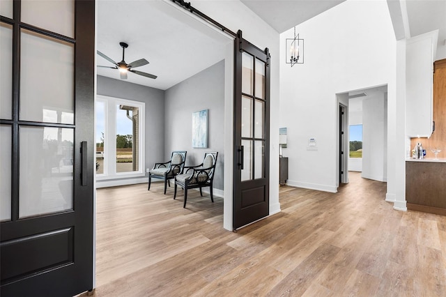 interior space with a barn door, light hardwood / wood-style floors, ceiling fan with notable chandelier, and high vaulted ceiling