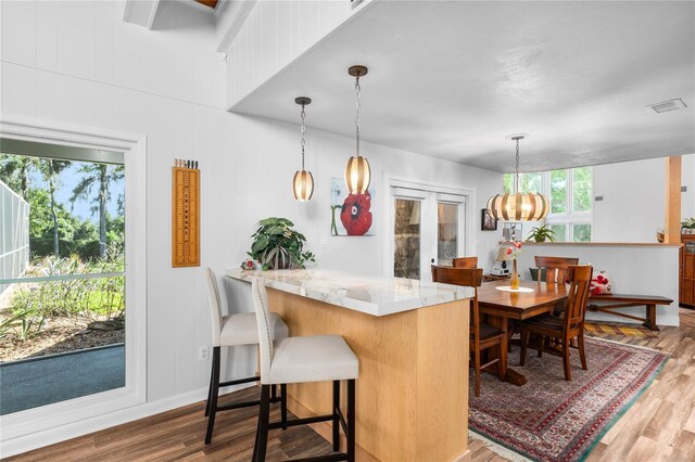 kitchen featuring hardwood / wood-style floors, kitchen peninsula, light stone countertops, and decorative light fixtures