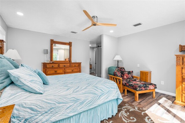 bedroom with a barn door, ceiling fan, and hardwood / wood-style flooring