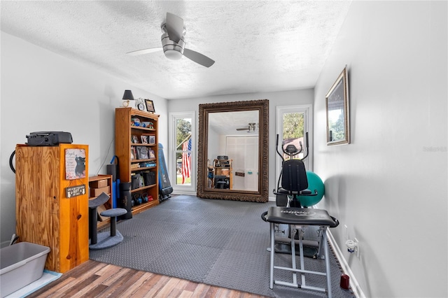 exercise room with hardwood / wood-style floors, ceiling fan, and a textured ceiling