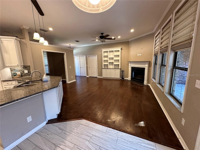 kitchen featuring hanging light fixtures, sink, light wood-type flooring, white cabinets, and tasteful backsplash