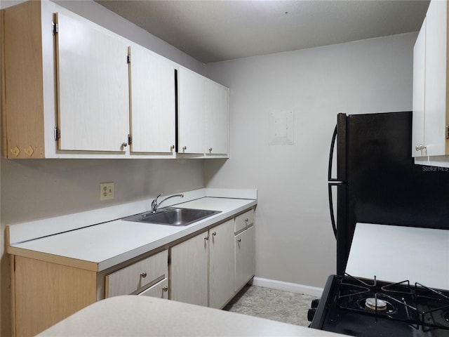 kitchen with black appliances, a sink, white cabinets, light countertops, and baseboards