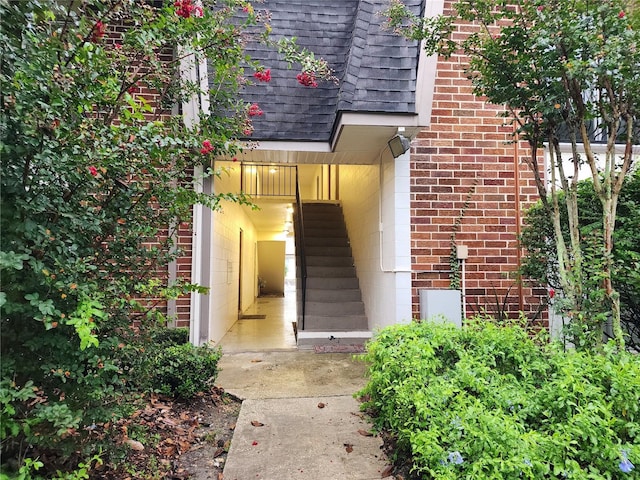 doorway to property with brick siding and roof with shingles