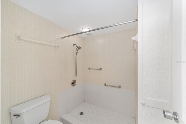 bathroom with toilet, a tile shower, and tile walls