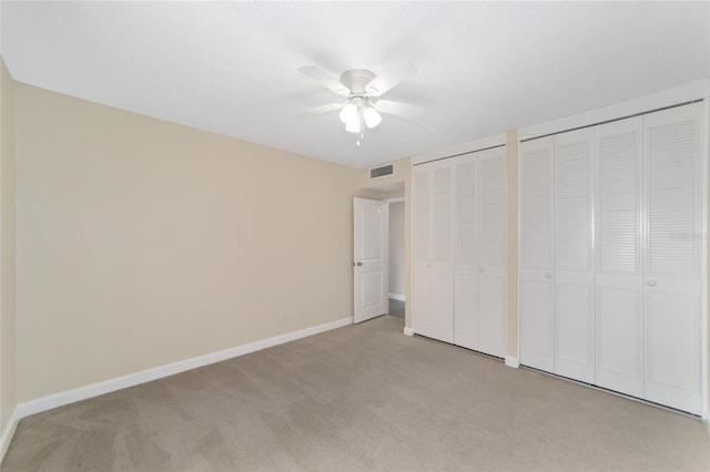 unfurnished bedroom with two closets, light colored carpet, and ceiling fan