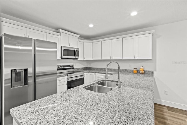 kitchen featuring kitchen peninsula, appliances with stainless steel finishes, light stone counters, sink, and white cabinetry