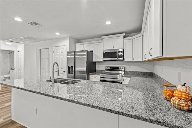 kitchen featuring dark stone counters, sink, kitchen peninsula, appliances with stainless steel finishes, and white cabinetry