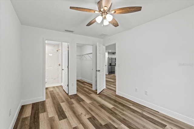 unfurnished bedroom with a walk in closet, ceiling fan, a closet, and hardwood / wood-style flooring