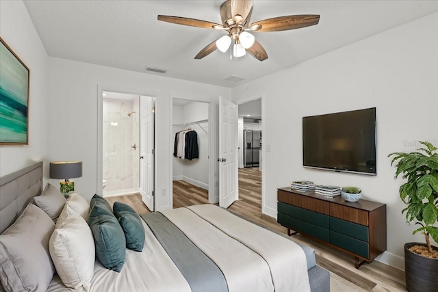 bedroom with ensuite bathroom, ceiling fan, a spacious closet, light wood-type flooring, and a closet