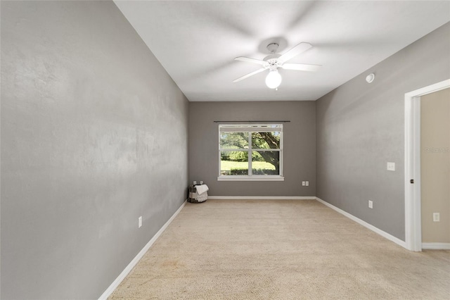 spare room featuring a ceiling fan, light carpet, and baseboards