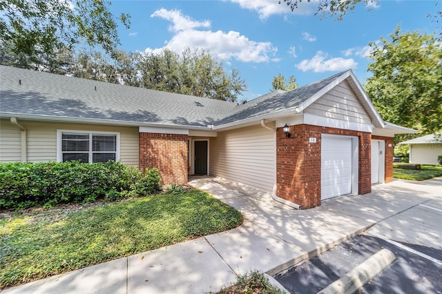 ranch-style house featuring an attached garage, a shingled roof, concrete driveway, and brick siding