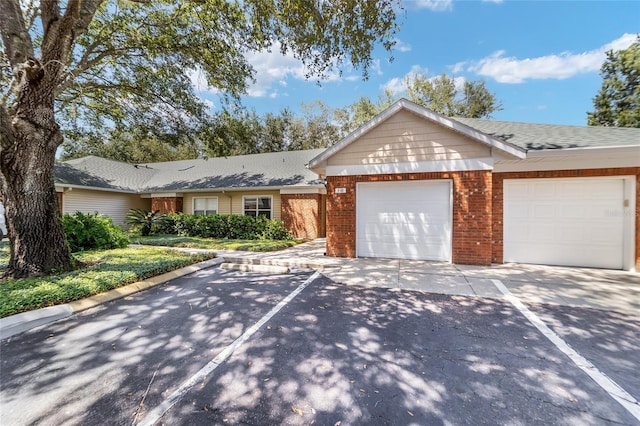 single story home featuring an attached garage, a shingled roof, concrete driveway, and brick siding