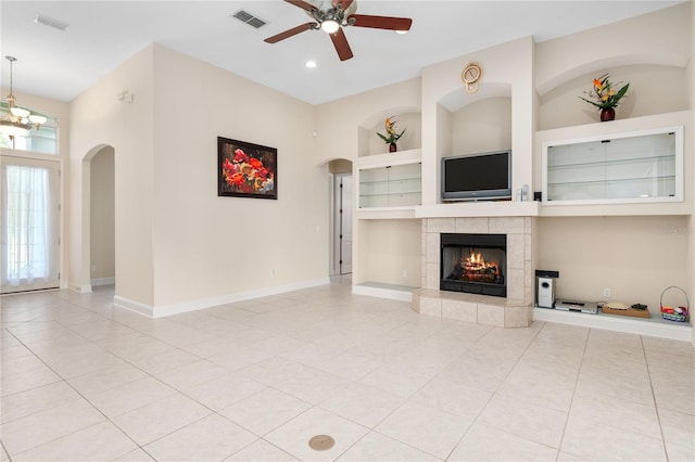 unfurnished living room with built in shelves, a tiled fireplace, ceiling fan with notable chandelier, and light tile patterned flooring