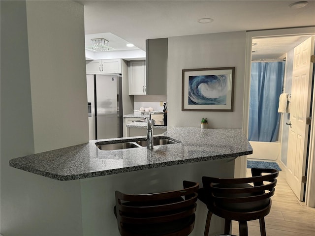 kitchen with sink, kitchen peninsula, stainless steel fridge with ice dispenser, white cabinetry, and a kitchen breakfast bar