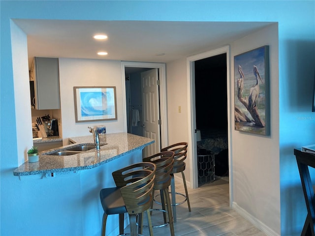 kitchen with light wood-type flooring, a breakfast bar area, sink, light stone counters, and kitchen peninsula