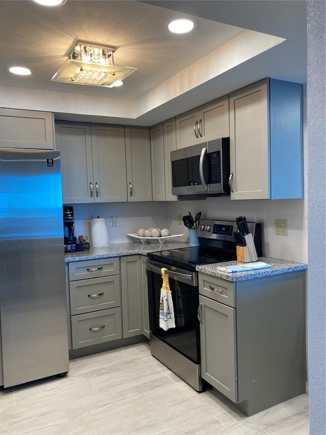 kitchen featuring light wood-type flooring, gray cabinetry, light stone counters, appliances with stainless steel finishes, and a textured ceiling