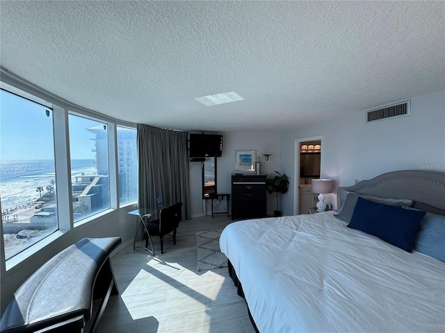 bedroom with a textured ceiling, a water view, and hardwood / wood-style flooring