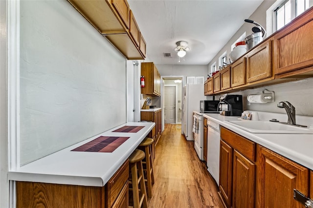 kitchen featuring white appliances, brown cabinetry, light wood-style flooring, light countertops, and a sink