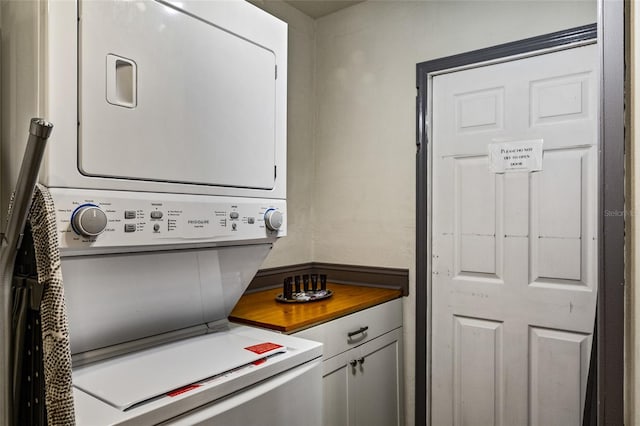 clothes washing area with stacked washing maching and dryer and cabinet space