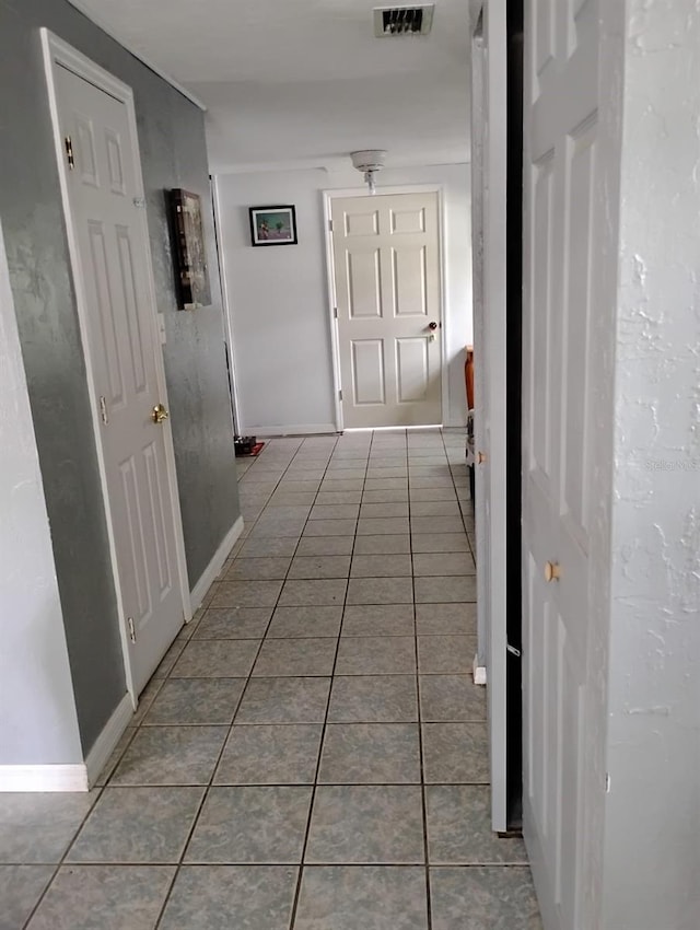 corridor with baseboards, visible vents, and tile patterned floors