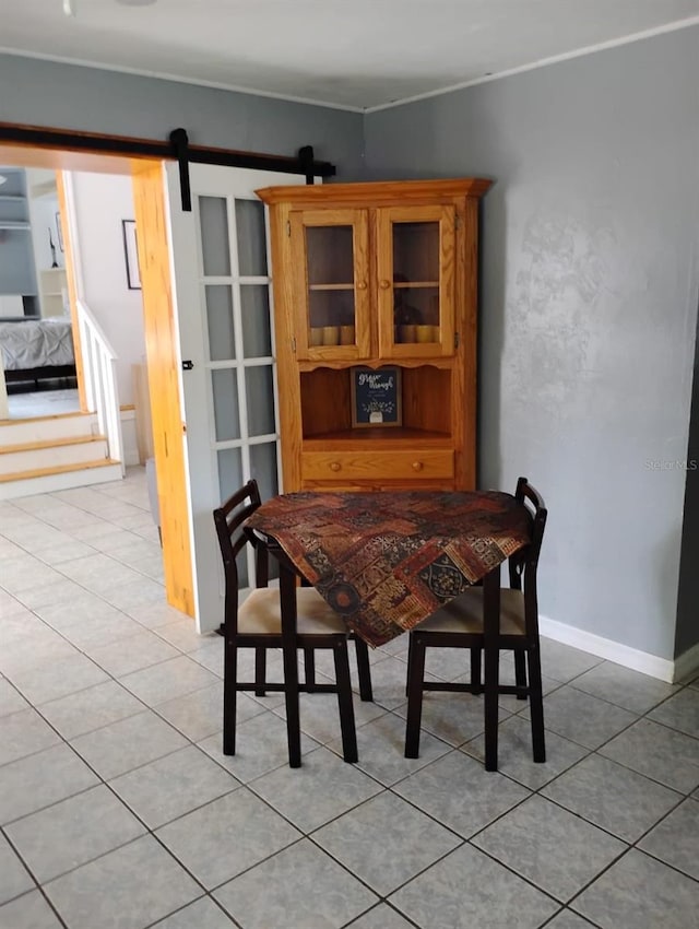 dining space with light tile patterned flooring, crown molding, baseboards, and a barn door