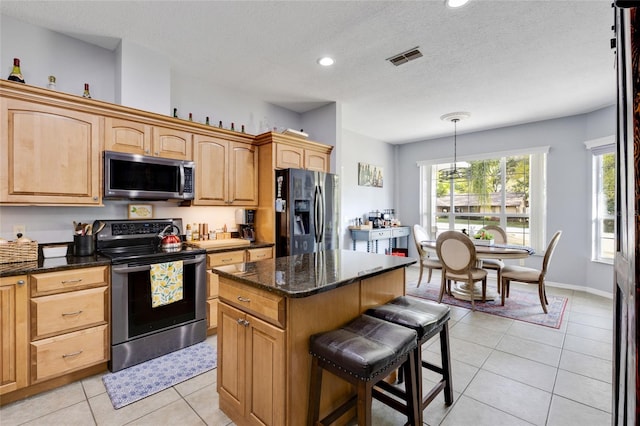 kitchen featuring dark stone countertops, decorative light fixtures, stainless steel appliances, a kitchen island, and a textured ceiling