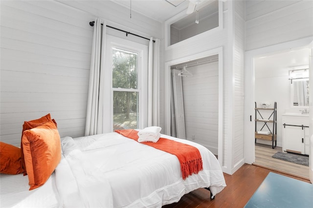 bedroom with a closet, hardwood / wood-style floors, and wood walls