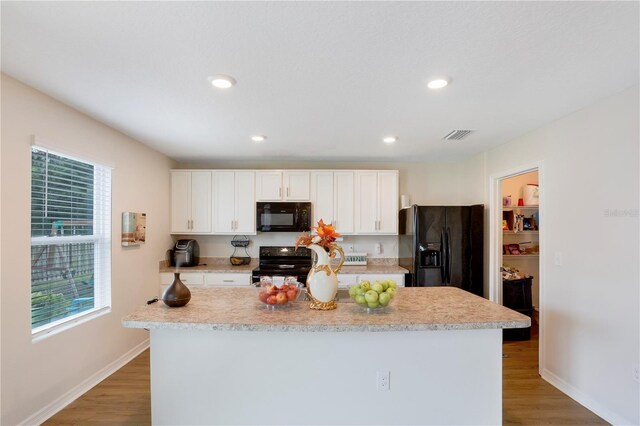 kitchen featuring black appliances, hardwood / wood-style floors, white cabinetry, and a kitchen island with sink