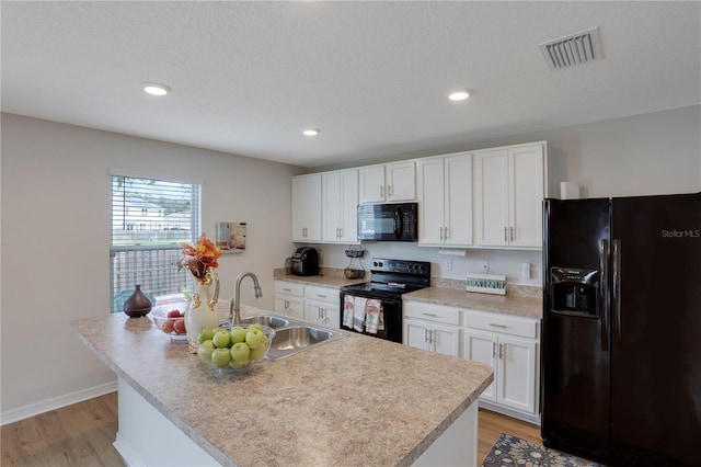 kitchen featuring sink, light hardwood / wood-style flooring, a center island with sink, white cabinetry, and black appliances