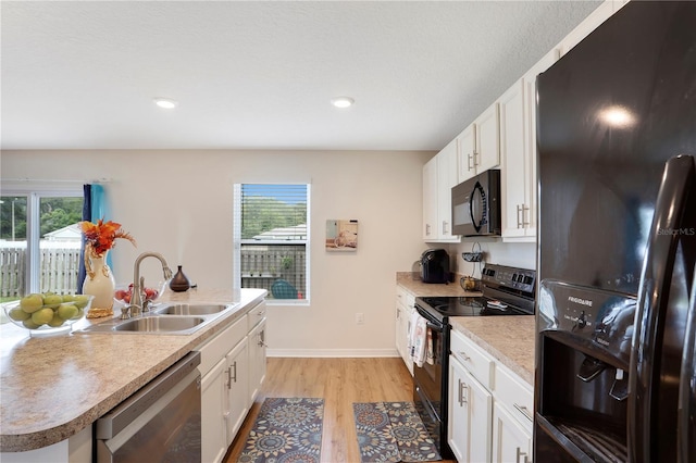 kitchen with sink, white cabinetry, light hardwood / wood-style flooring, black appliances, and a center island with sink