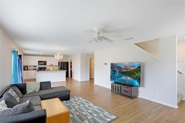 living room with light wood-type flooring, ceiling fan with notable chandelier, and a textured ceiling