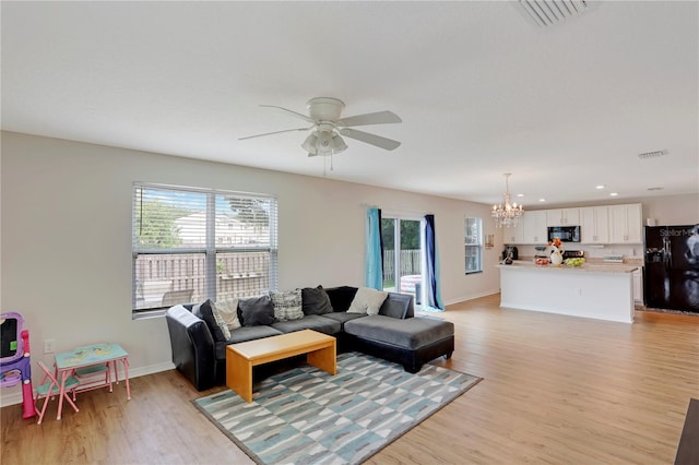 living room featuring ceiling fan with notable chandelier and light wood-type flooring