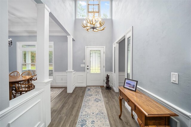 entryway featuring hardwood / wood-style flooring, a notable chandelier, ornate columns, a high ceiling, and ornamental molding