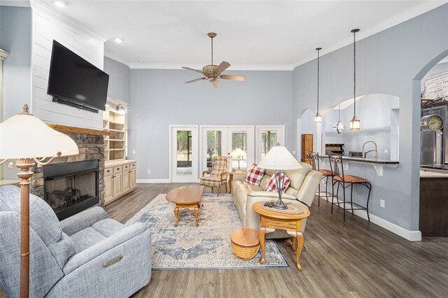 living room with ornamental molding, dark wood-type flooring, ceiling fan, and a stone fireplace