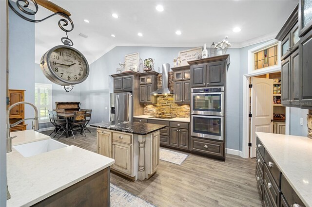 kitchen with a center island, sink, wall chimney exhaust hood, hardwood / wood-style flooring, and appliances with stainless steel finishes