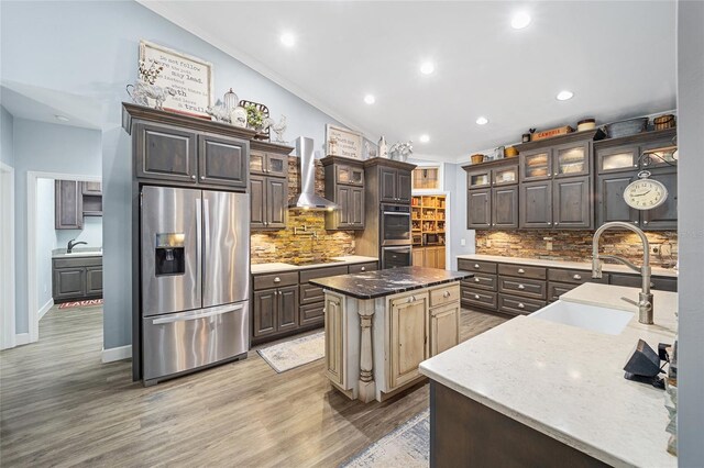 kitchen featuring backsplash, appliances with stainless steel finishes, sink, wall chimney exhaust hood, and an island with sink