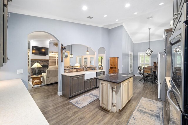 kitchen with a center island, decorative light fixtures, dark hardwood / wood-style floors, a stone fireplace, and ornamental molding