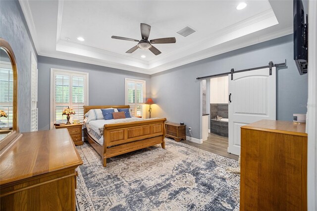 bedroom with crown molding, a barn door, light hardwood / wood-style floors, ceiling fan, and connected bathroom