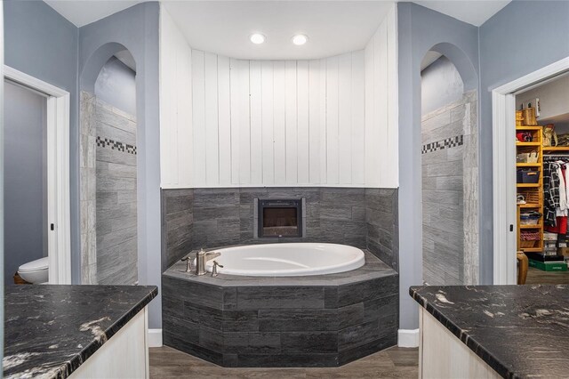 bathroom with tiled tub, vanity, toilet, and hardwood / wood-style floors