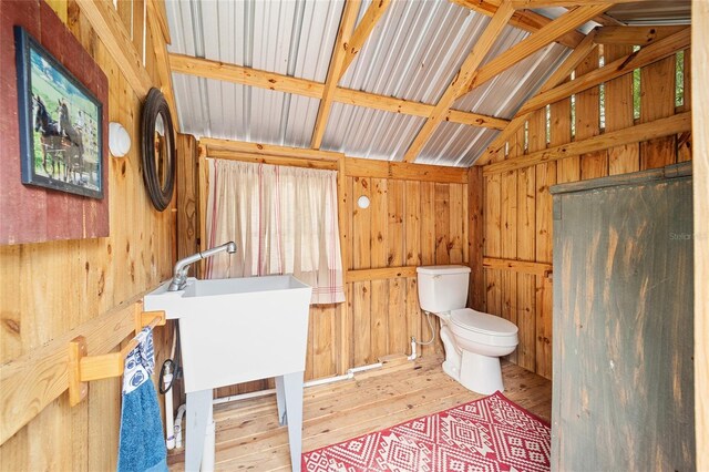 bathroom with wood walls, wood-type flooring, toilet, and vaulted ceiling with beams