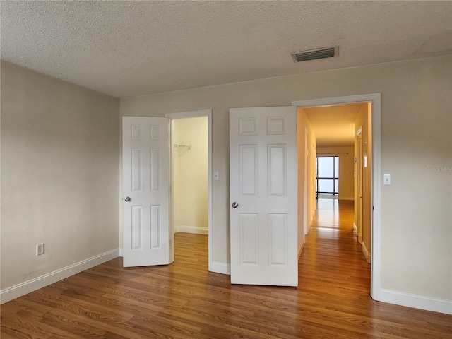 unfurnished bedroom featuring dark hardwood / wood-style flooring, a spacious closet, a textured ceiling, and a closet