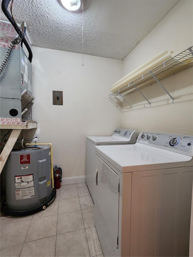 clothes washing area featuring light tile patterned flooring, electric water heater, independent washer and dryer, and a textured ceiling